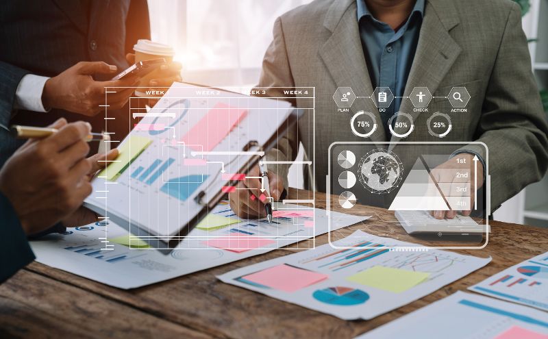 Geschäftsleute arbeiten an einem Tisch sitzend mit Klemmbrettern und Papierausdrucken an Statistiken