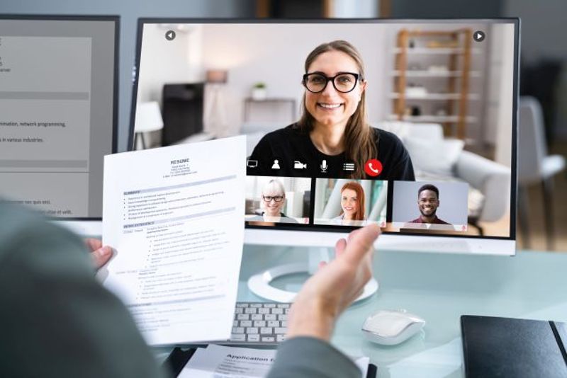 Mehrere Personen unterhalten sich in einer Videokonferenz online. Die Person im Bild hält Geschäftsunterlagen in der Hand.