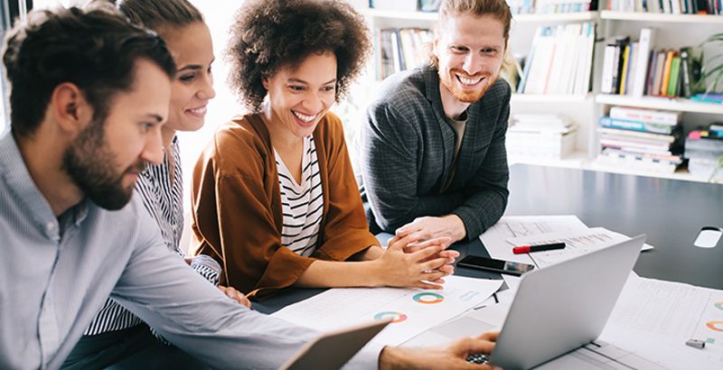 Eine Gruppe von Menschen arbeitet gemeinsam fröhlich lächelnd vor dem Laptop